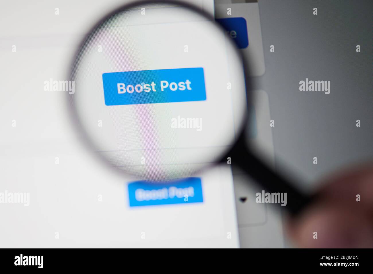 New-York , USA - March 13, 2020: Boost post on social media on laptop close up view throw magnifier Stock Photo
