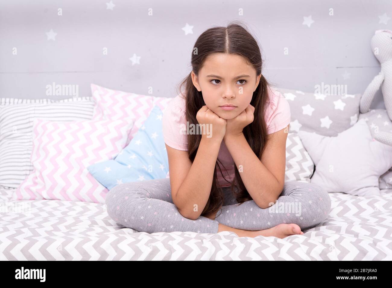 Unhappy cutie. Unhappy baby sit in bed. Little child with unhappy look. Bedtime routine. Daytime nap. Kids health. Childcare. Early morning. Good night. I cant sleep when Im unhappy. Stock Photo