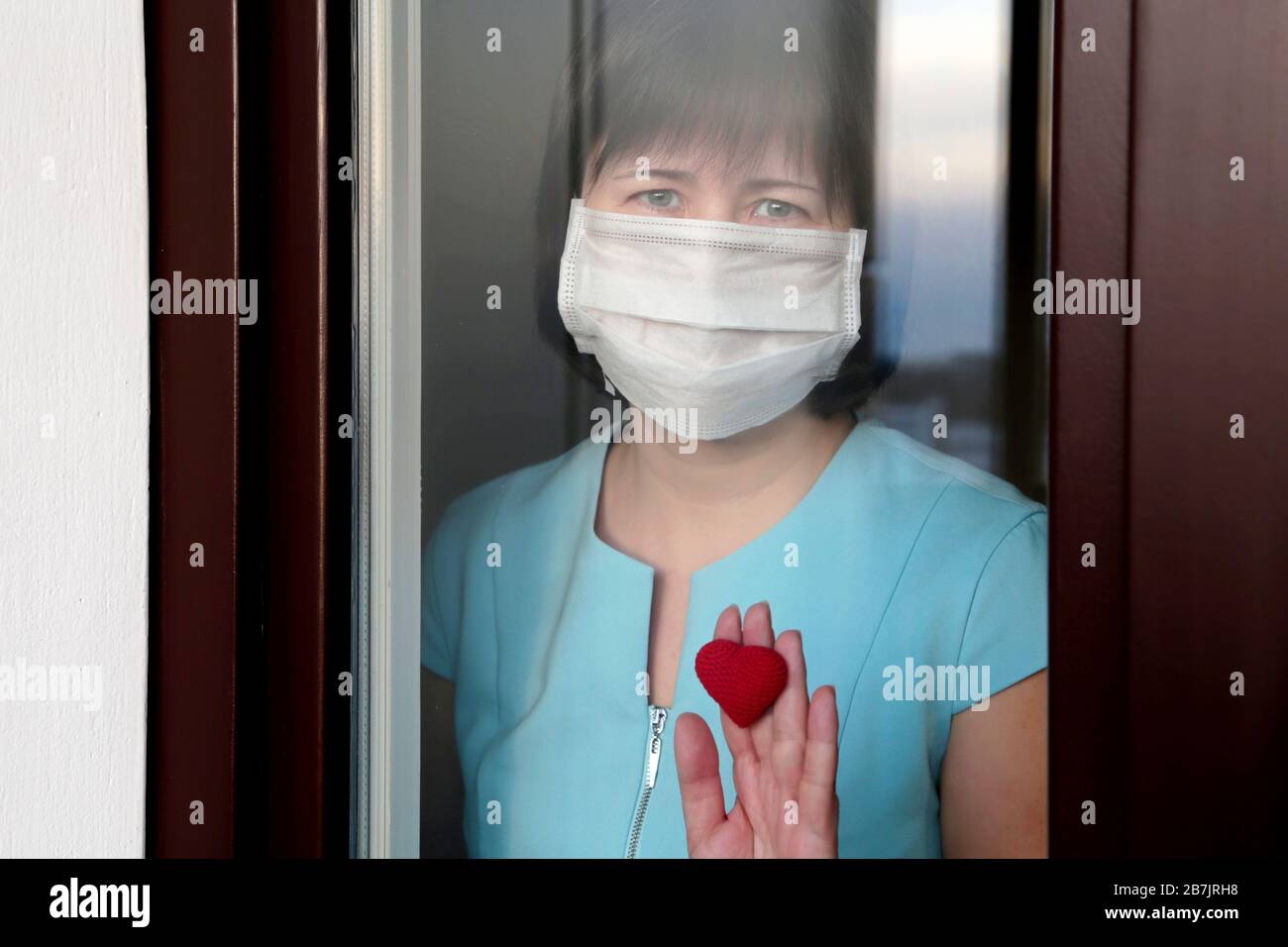 Coronavirus quarantine during the COVID-19 epidemic. Sad woman in a medical mask looks out of the window Stock Photo