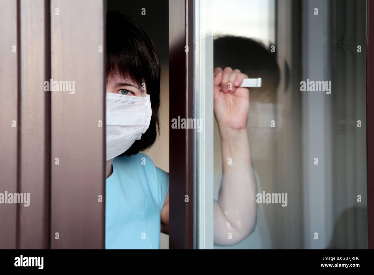 Coronavirus quarantine during the COVID-19 epidemic. Sad woman in a medical mask looks out of the window Stock Photo