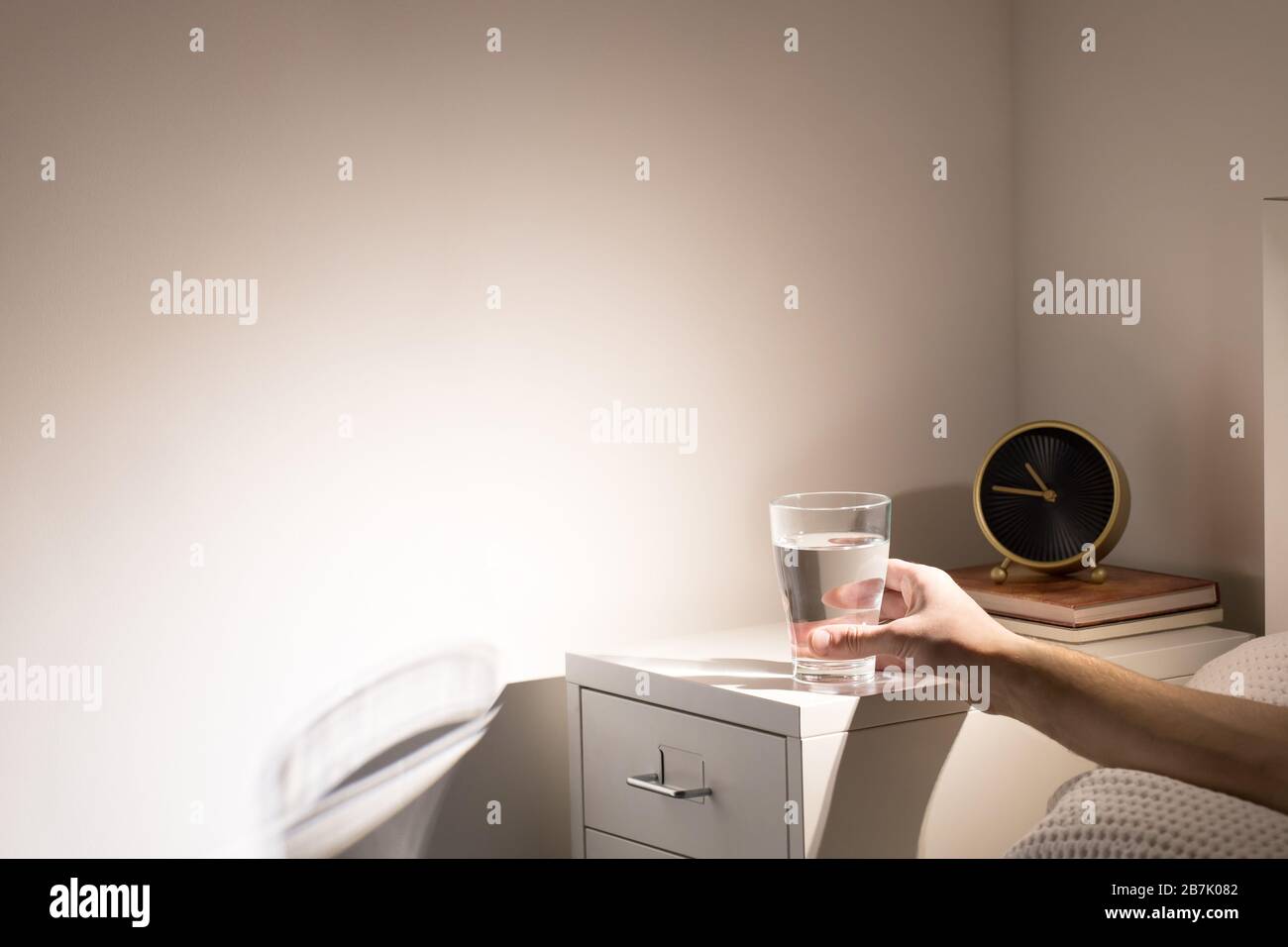 Good habit - drinking a glass of water before going to sleep. Man in bed taking glass of water from bedside table before bedtime, copy space. Stock Photo