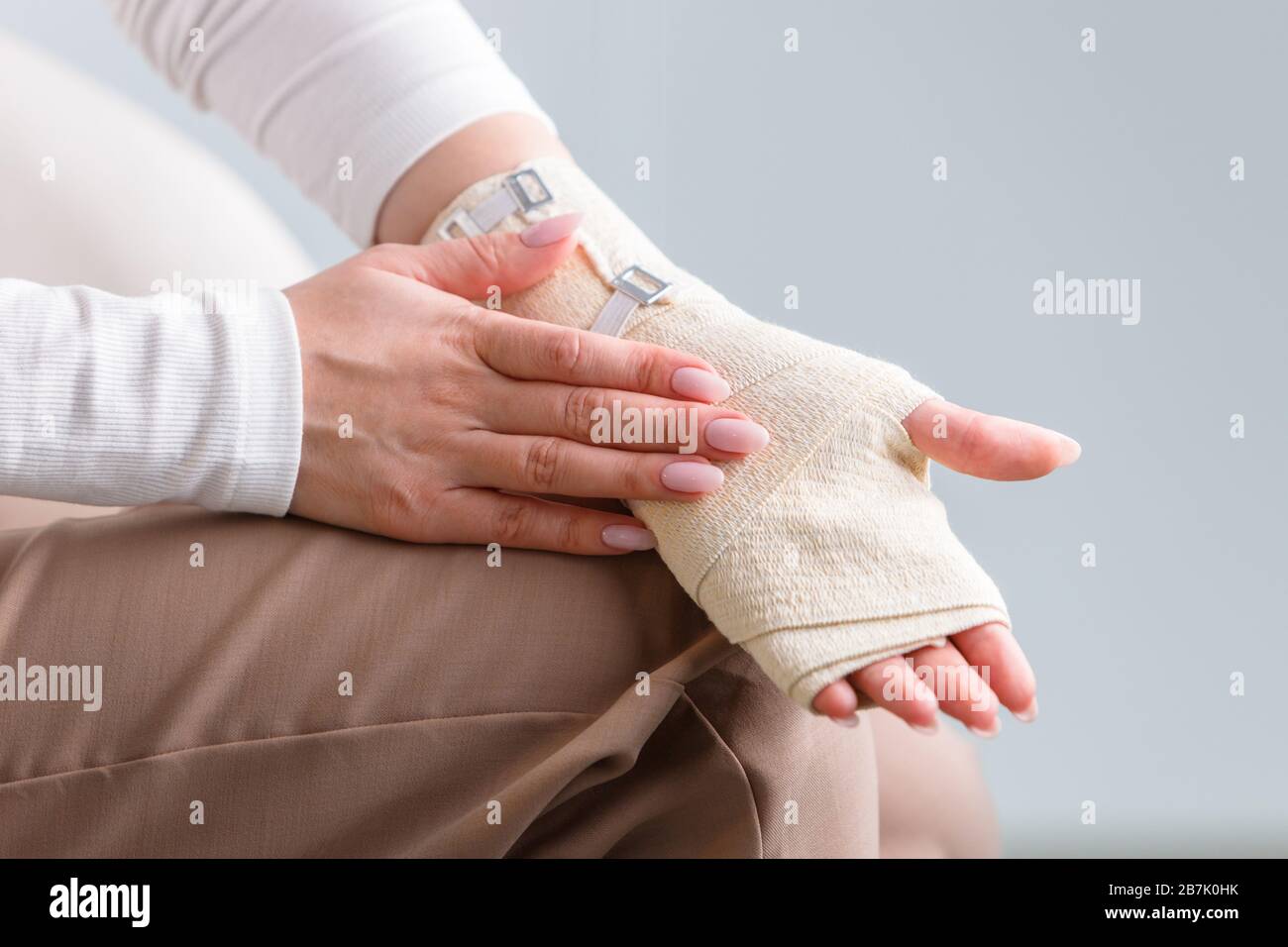 Woman touching her wrapped painful wrist with flexible elastic supportive orthopedic bandage after unsuccessful sports or injury, close up. Carpal tun Stock Photo