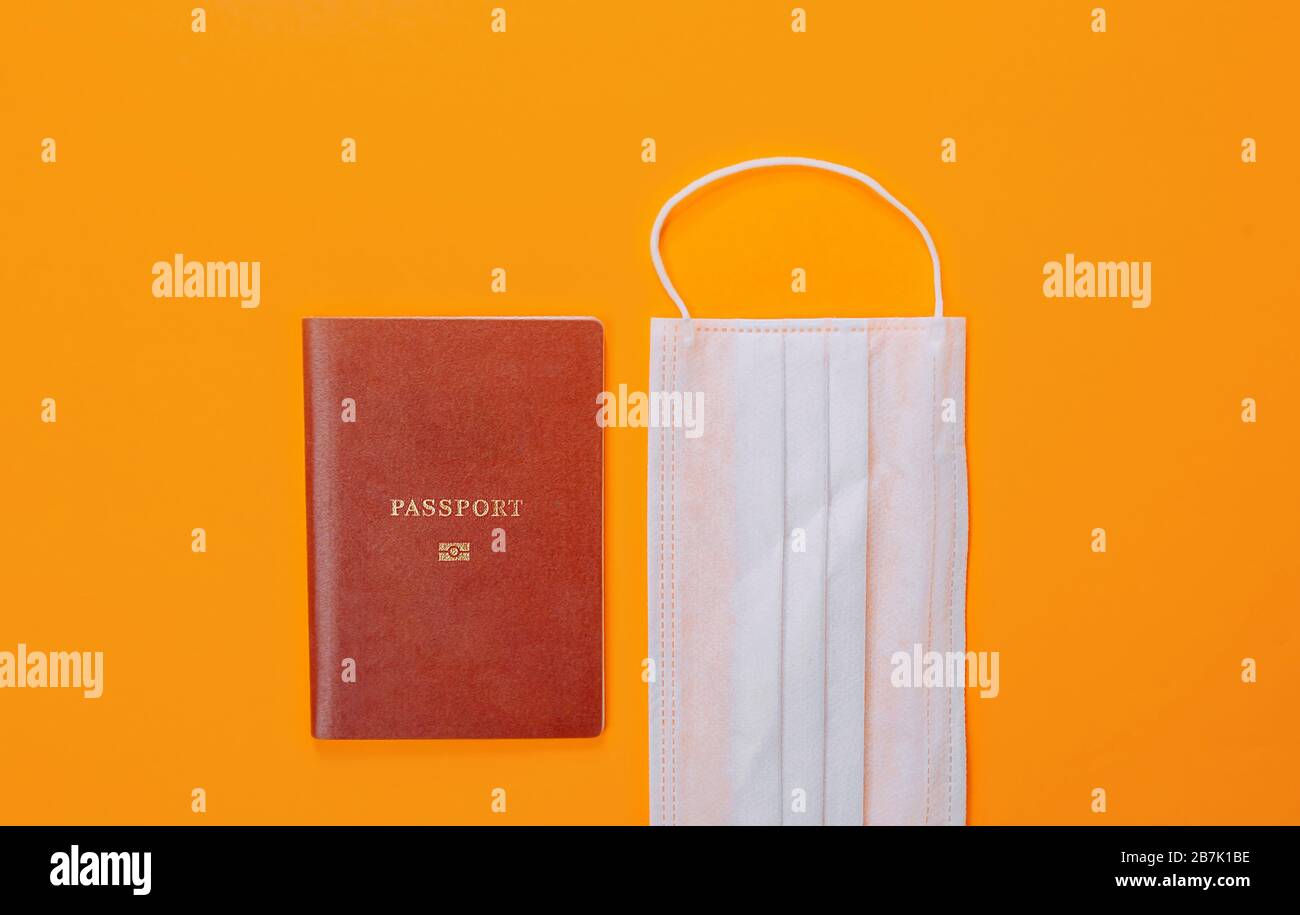 A red international passport and a blue medical surgical mask for protection against coronavirus are next to each other on a bright orange background. Stock Photo