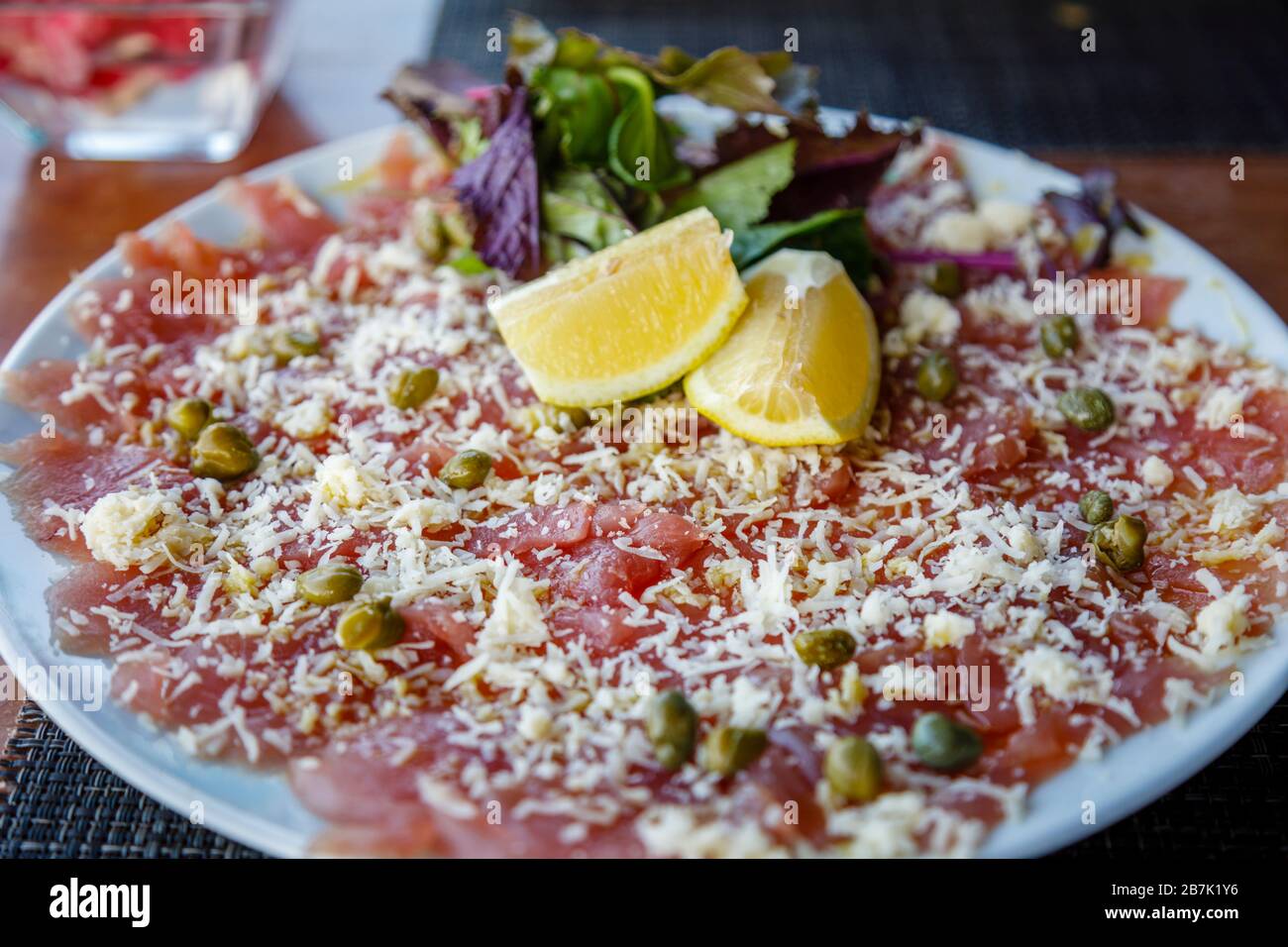 Plate of yellow fin tuna carpaccio garnished with grated cheese, capucine capers and lemon slices, in a restaurant in Hanga Roa, Easter Island Stock Photo