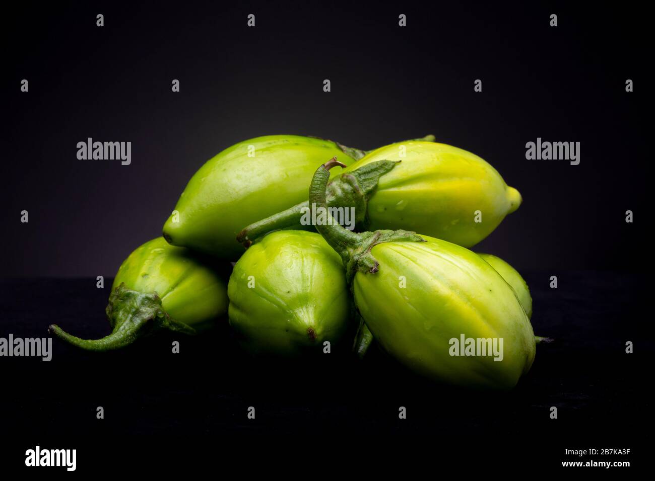 Vibrant green lot of scarlet eggplant vegetable grouped together on dark background Stock Photo