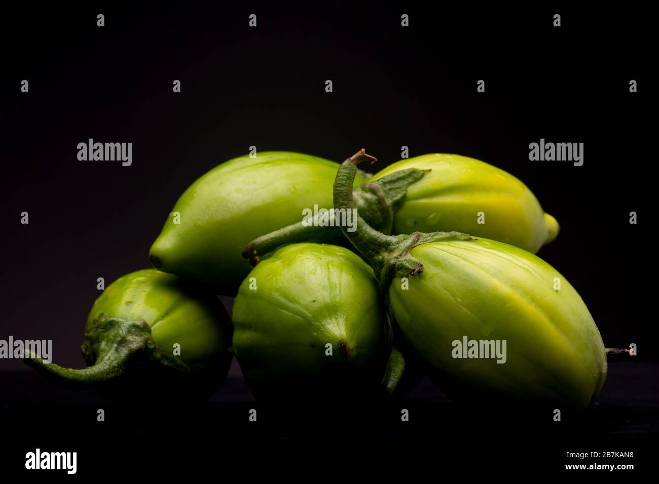 Vibrant green lot of scarlet eggplant vegetable grouped together on dark background Stock Photo