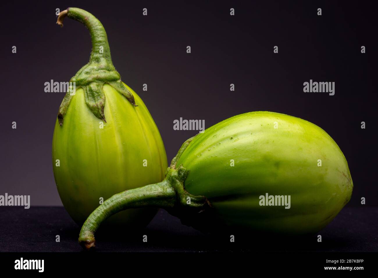 Lot of lot of vibrant green scarlet eggplant vegetable on top of each other  against a black background. Graphic minimalist image of food. Stock Photo