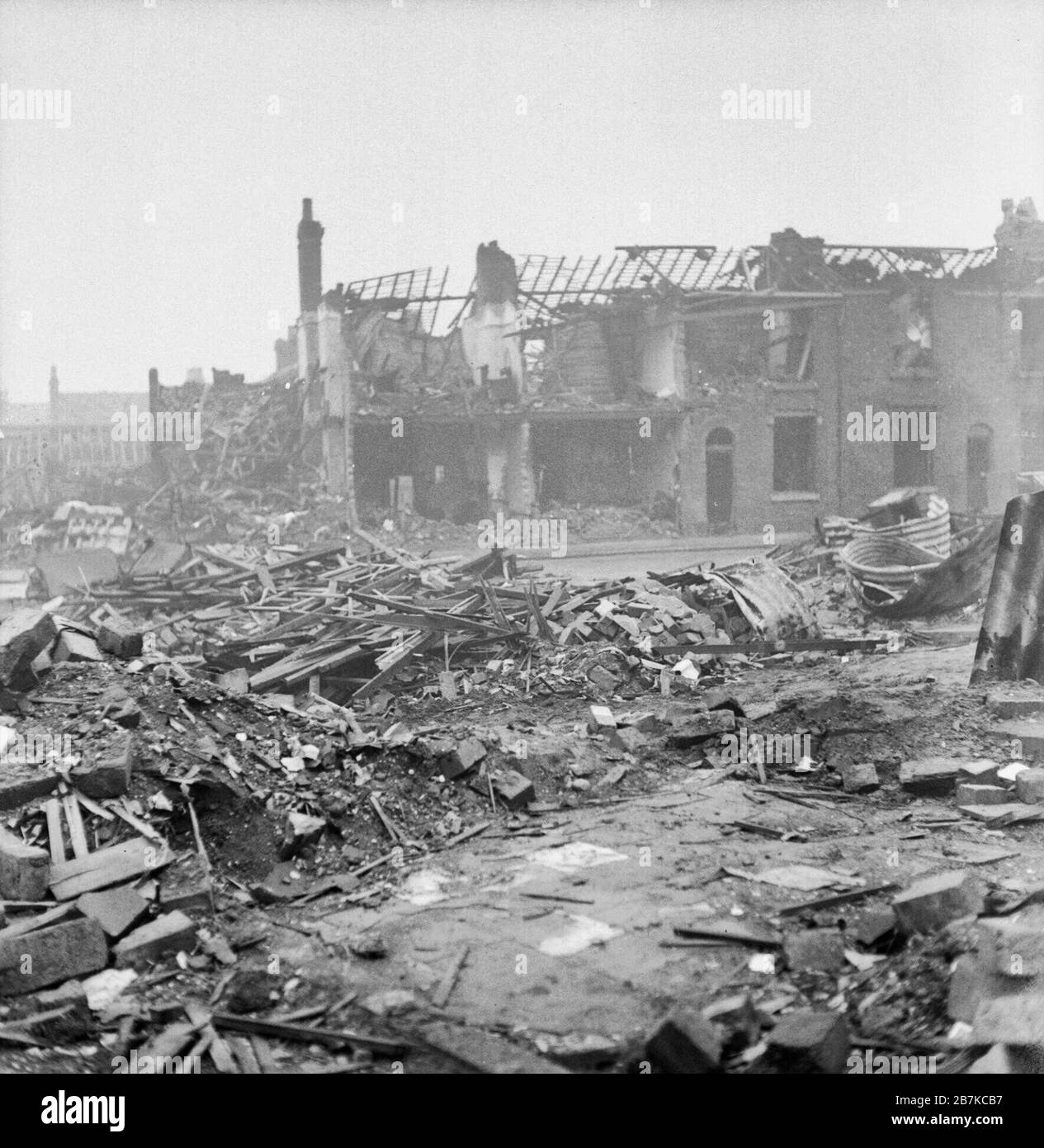 Bomb Damage in Birmingham, England, C 1940 Although some debris has been cleared on this site on James Street, Aston Newtown, Birmingham, a large pile of timbers and some brick rubble can be clearly seen. Also visible to the right of the photograph are the twisted remains of several Anderson shelters. In the background, two of the terraced houses that are still standing have had the front wall stripped away by the blast, revealing the interior walls and floors. Stock Photo