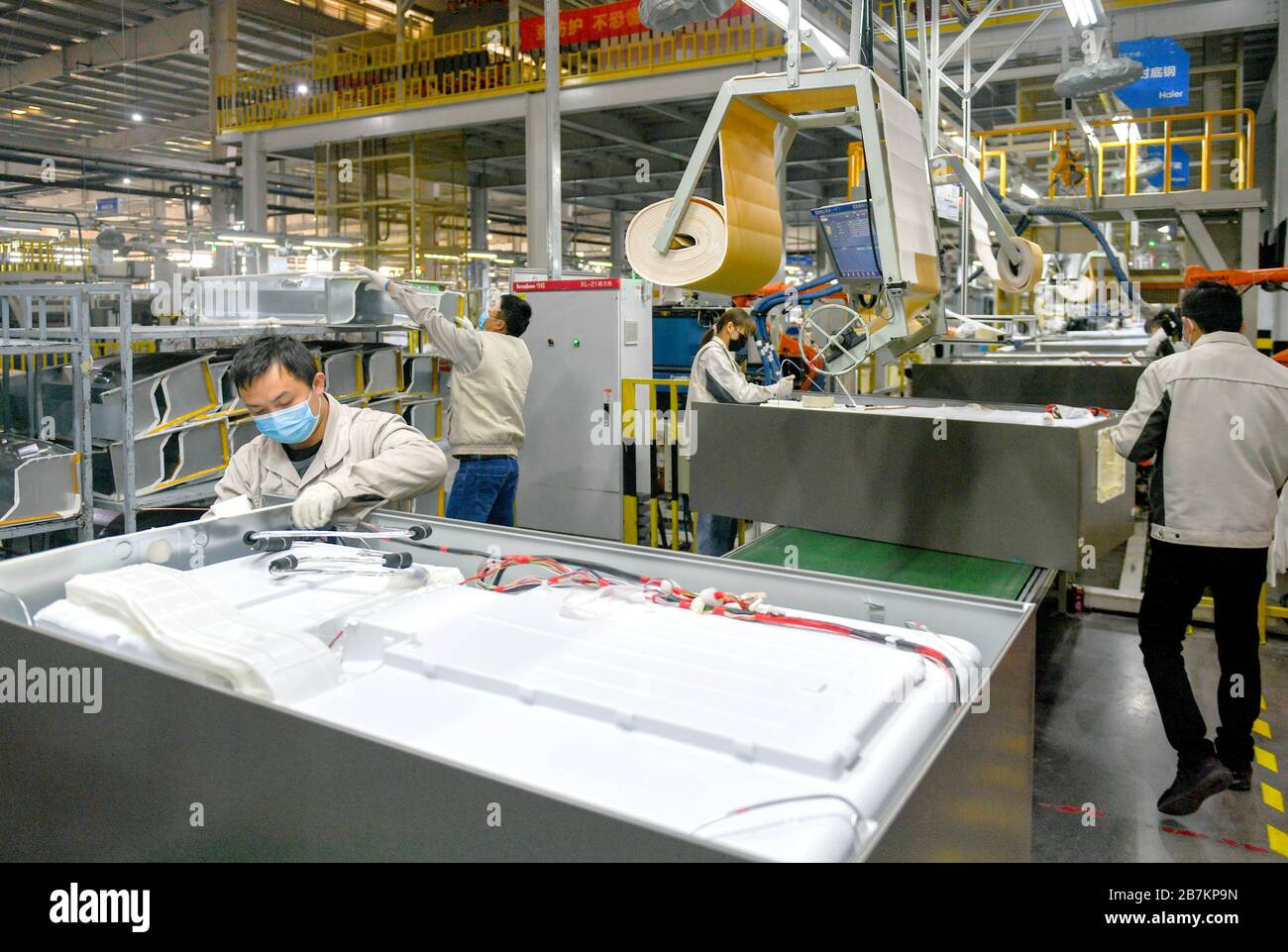 Workers with mask on control the machine to product at a local factory of Haier Group Corporation, a multinational home appliances and consumer electr Stock Photo