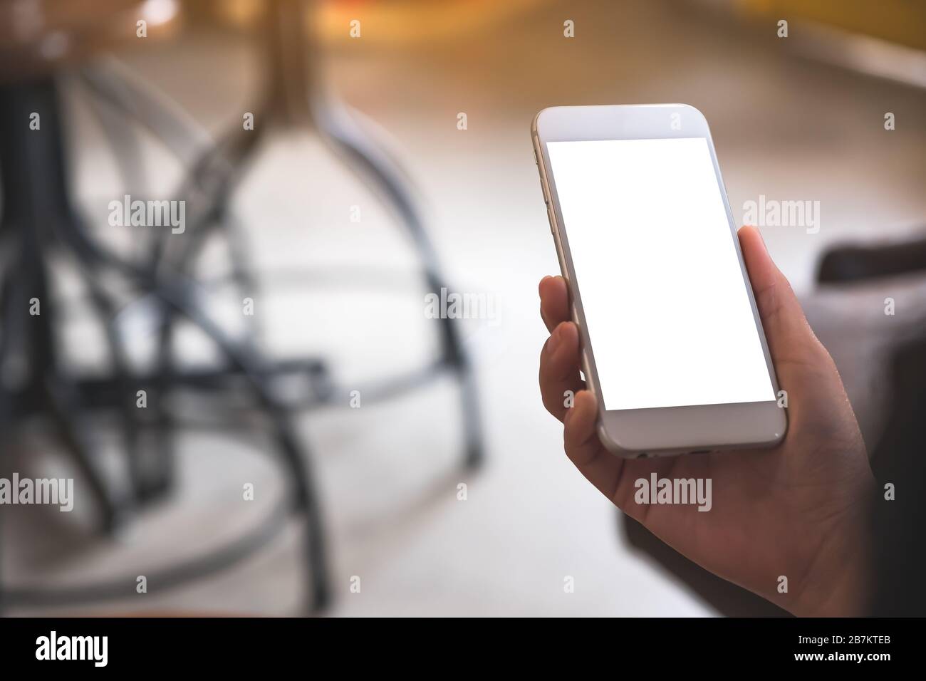 Mockup image of a hand holding white mobile phone with blank desktop