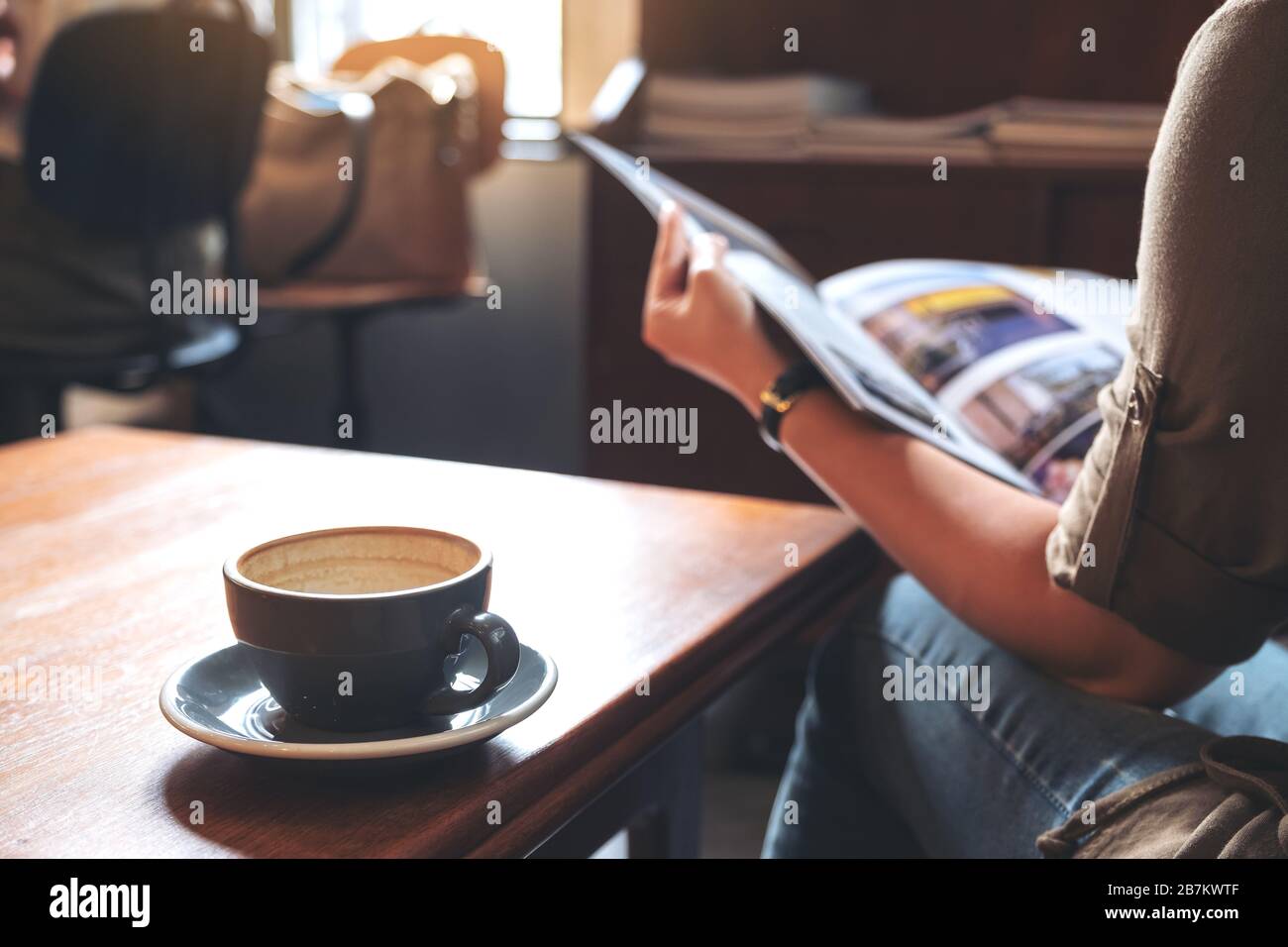 Closeup image of a woman reading a book with coffee cup on wooden table in modern cafe Stock Photo