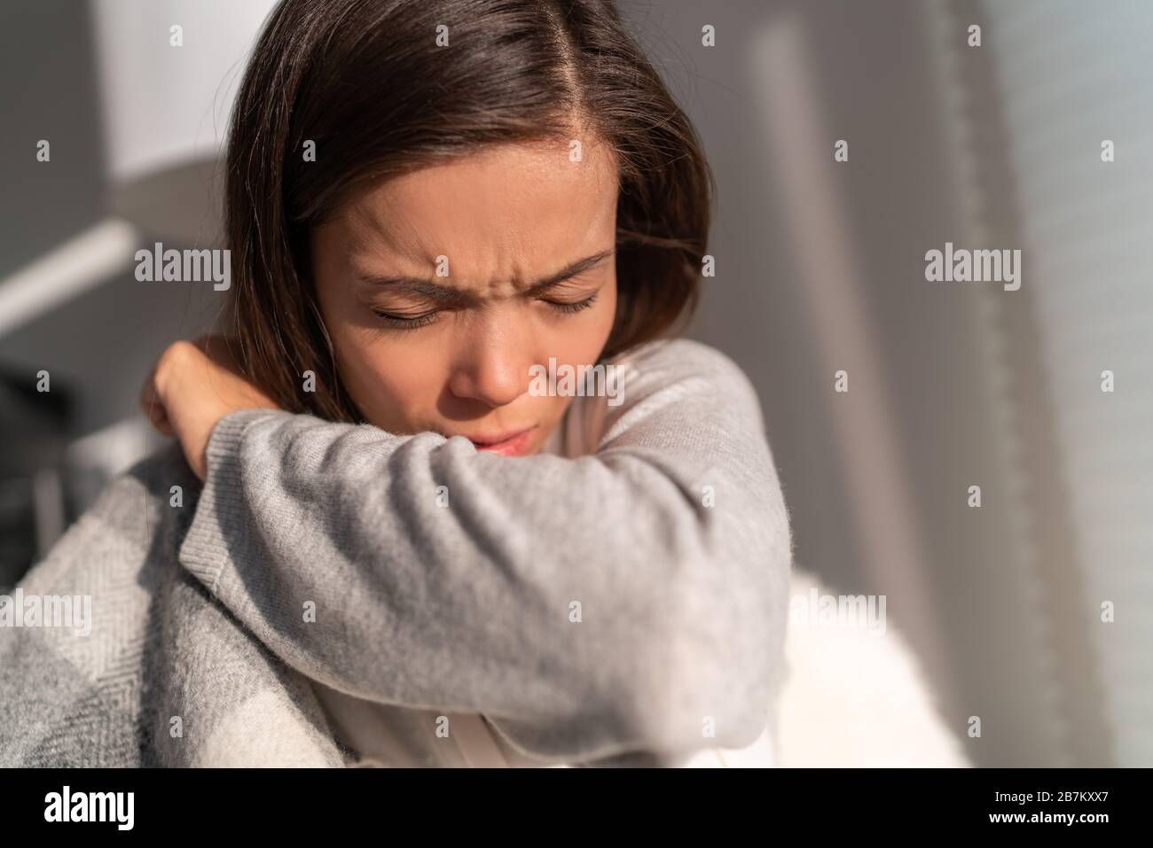 Coronavirus COVID-19 reducing of risk of spreading the infection by covering nose and mouth when coughing and sneezing with tissue or flexed elbow. Asian woman cough in arm prevention. Stock Photo