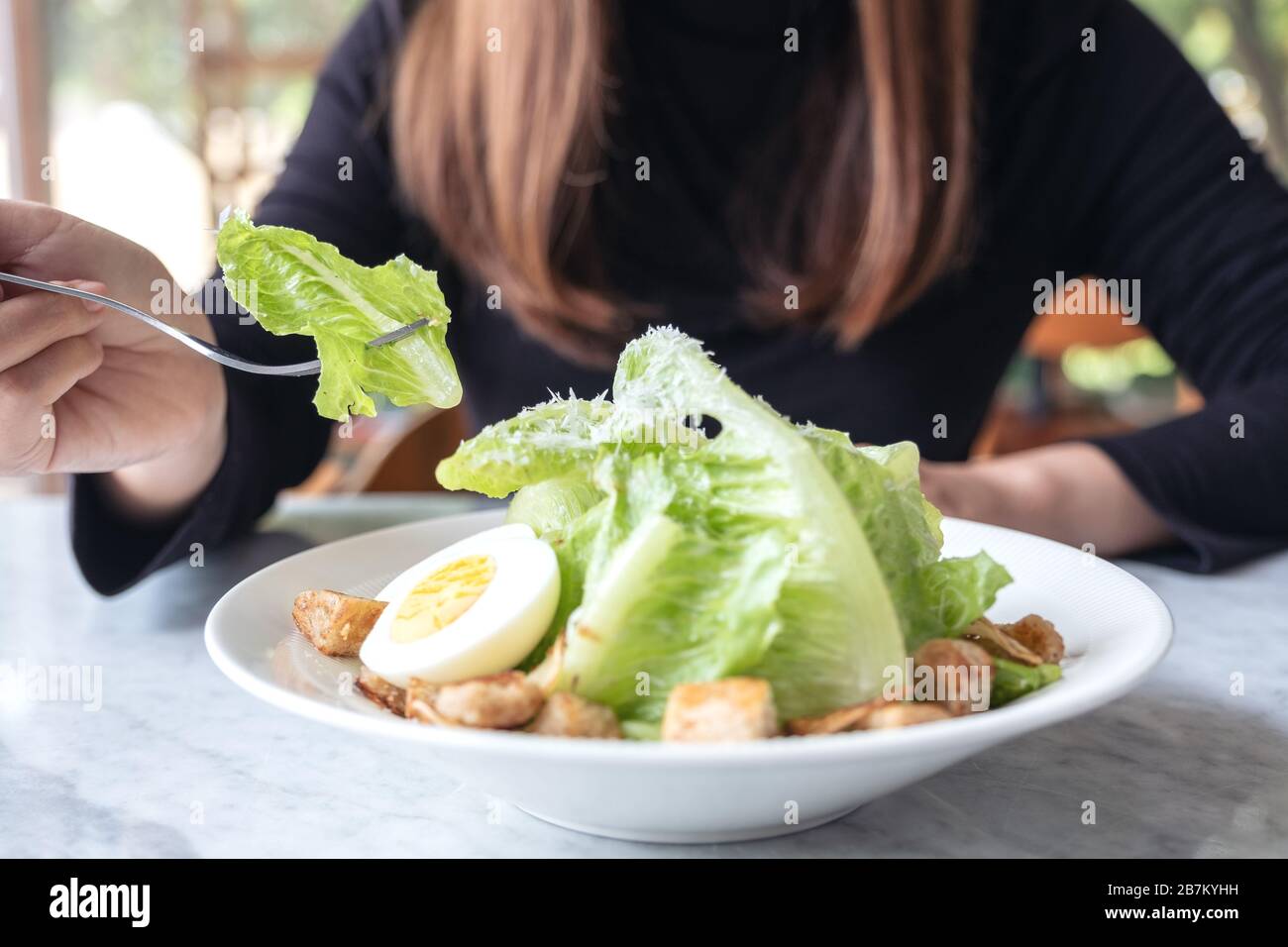 Closeup image of a woman eating caesar salad by fork on table in the