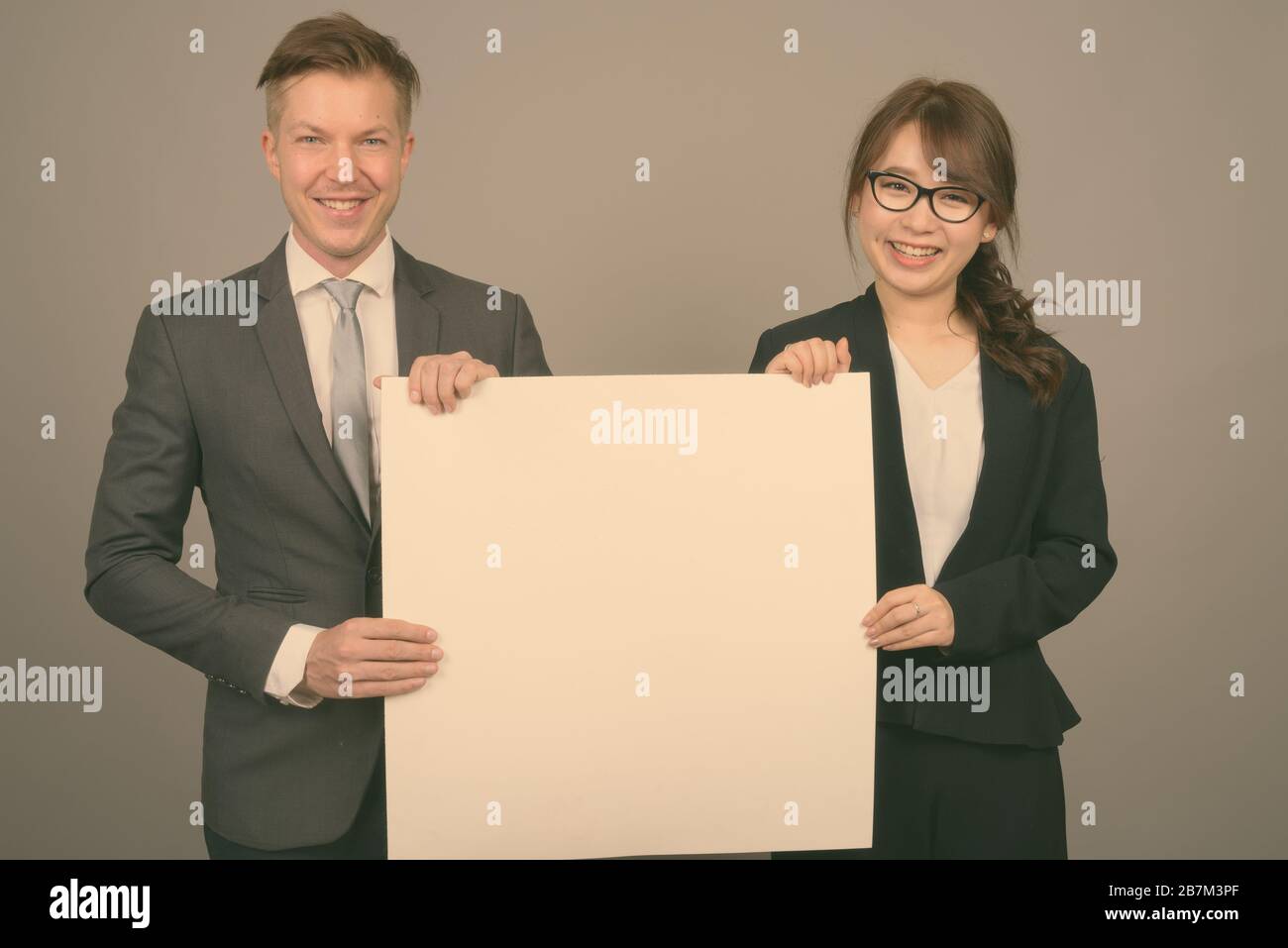Studio shot of young handsome businessman and young beautiful Asian businesswoman wearing eyeglasses against gray background Stock Photo