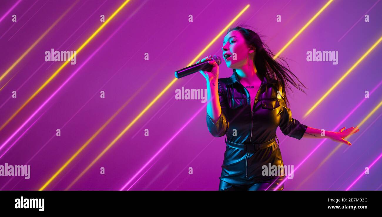 Creative emotions and neon lines on purple background, flyer, proposal. Caucasian young woman, musician singing. Concept of human emotions, facial expression, sales, ad, music, hobby. Modern art. Stock Photo
