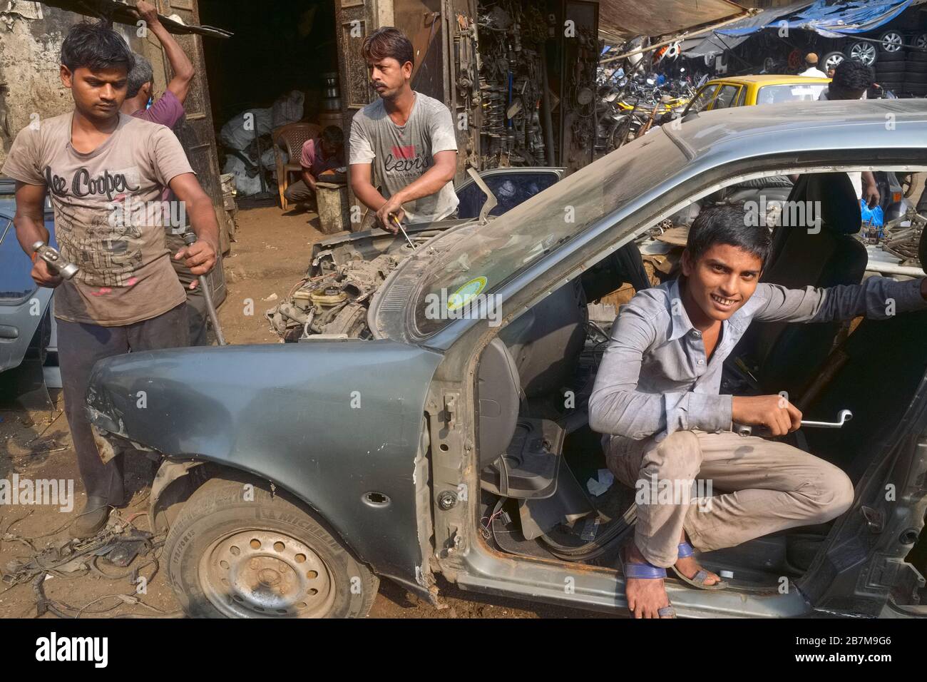 Three workers are dismantling a car wreck, its parts to be sold as scrap metal; at Chor Bazar (Thieves' Market), Bhendi Bazar, Mumbai, India Stock Photo