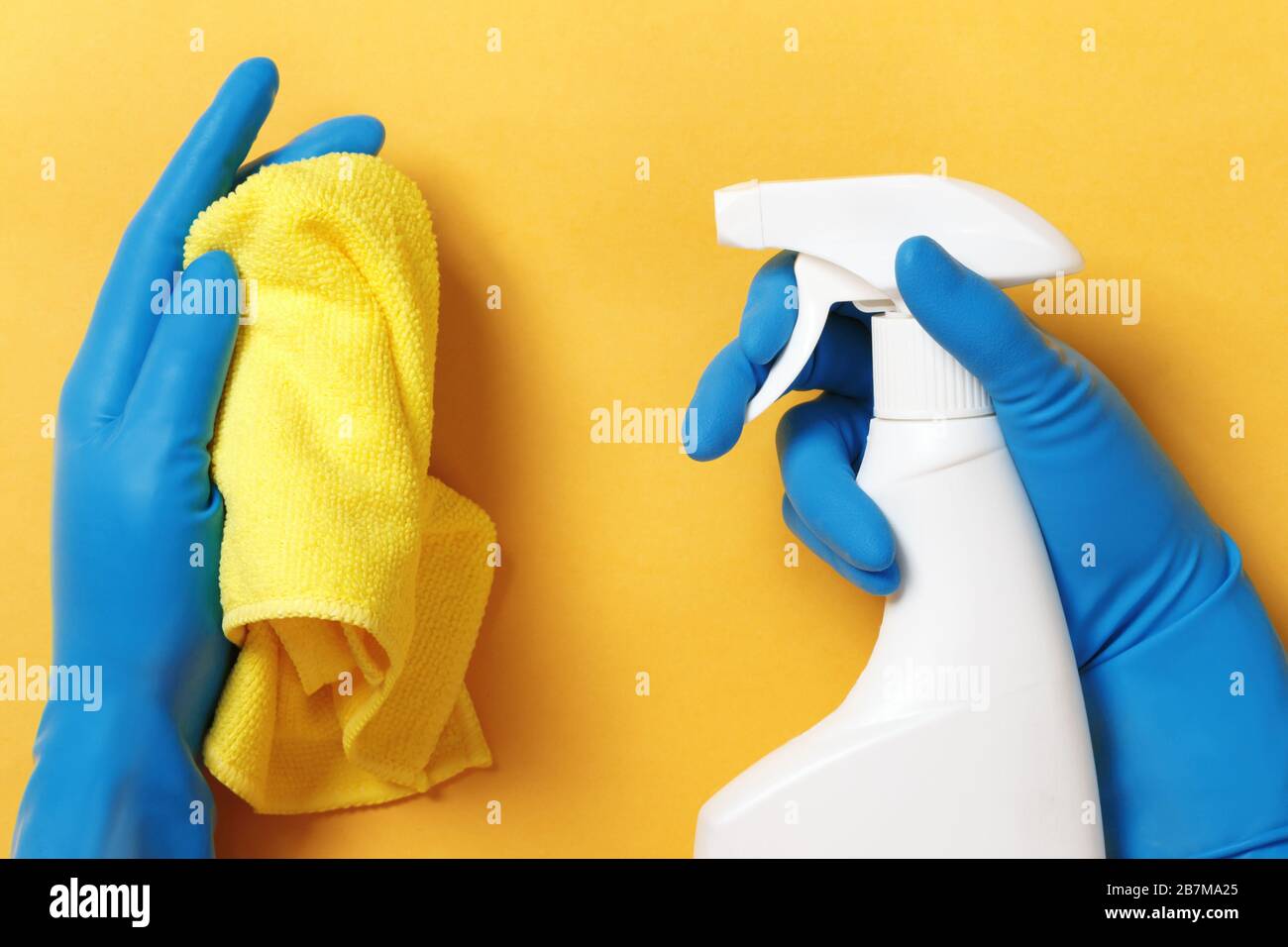 Hands in protective rubber gloves holding a spray bottle with detergent ...