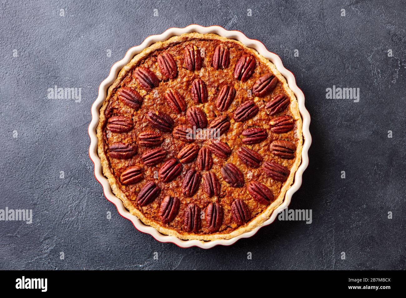 Pecan pie, tart in baking dish. Traditional festive Thanksgiving dessert. Dark background. Top view. Stock Photo