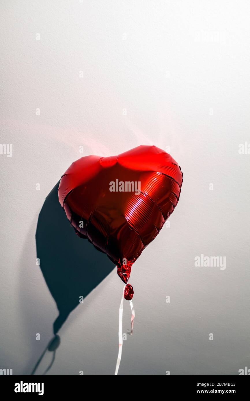 Heart shaped red helium balloon with a tie, hit to a white ceiling with shadow. Stock Photo