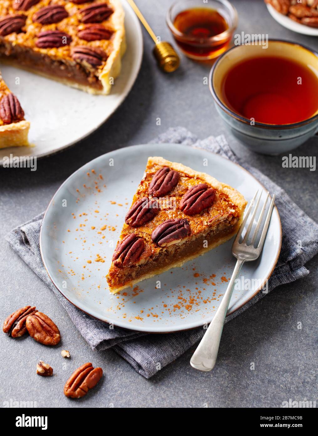 Pecan pie, tart slice on a plate with cup of tea. Grey background. Stock Photo