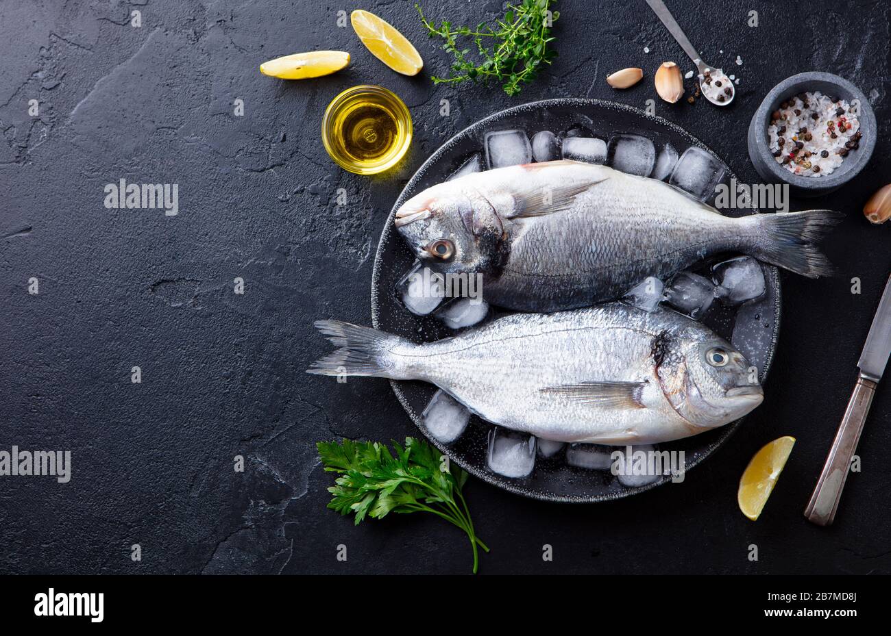 Dorado raw fish on a plate with ice and lemon. Black slate background. Copy space. Top view. Stock Photo