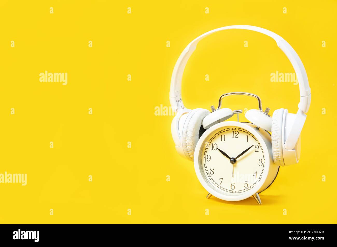 White alarm clock and headphones on a yellow background. Music. Relaxation. Place for text Stock Photo