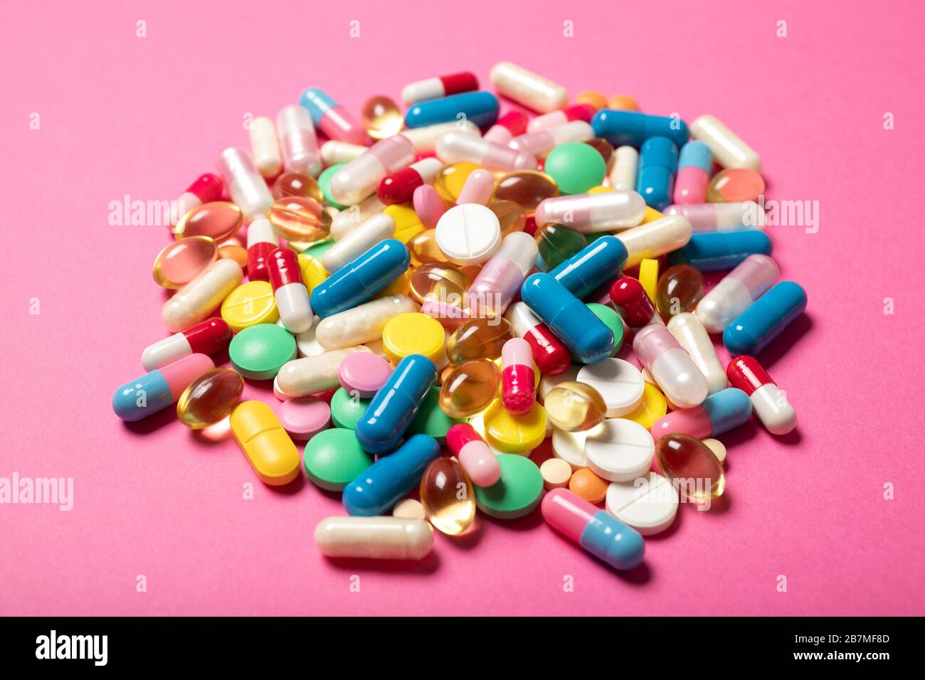 A lot of multi-colored pills on a pink background. Stock Photo