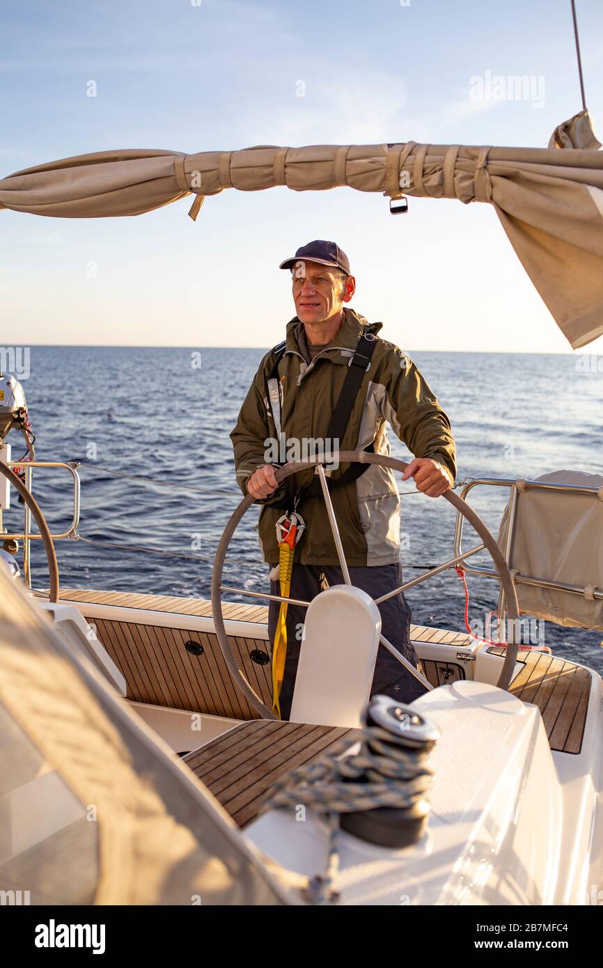 Mature sailor at steering wheel, Mast, boom and ropes. View from a