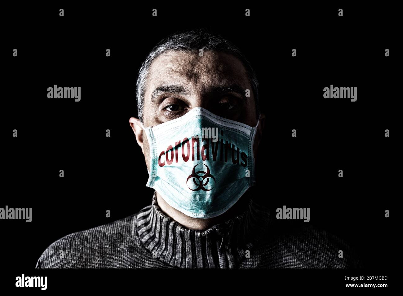 Man with surgical mask. Biohazard and Coronavirus, aka COVID-19 symbol. Pandemic or epidemic and scary, fear or danger concept. Black Background Stock Photo