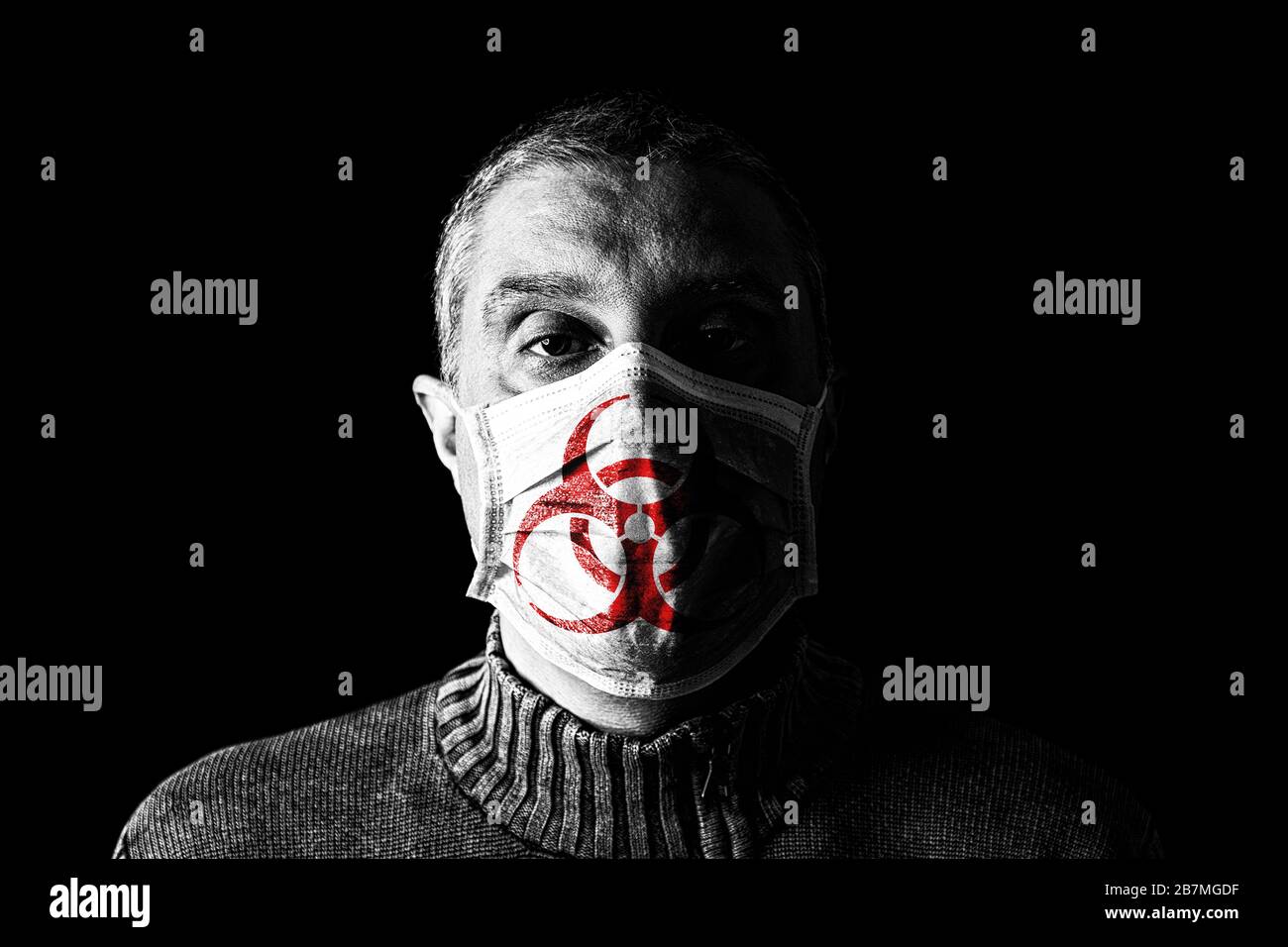 Man with surgical mask with biohazard or biological hazard symbol. Pandemic or epidemic and scary, fear or danger concept. Black Background Stock Photo