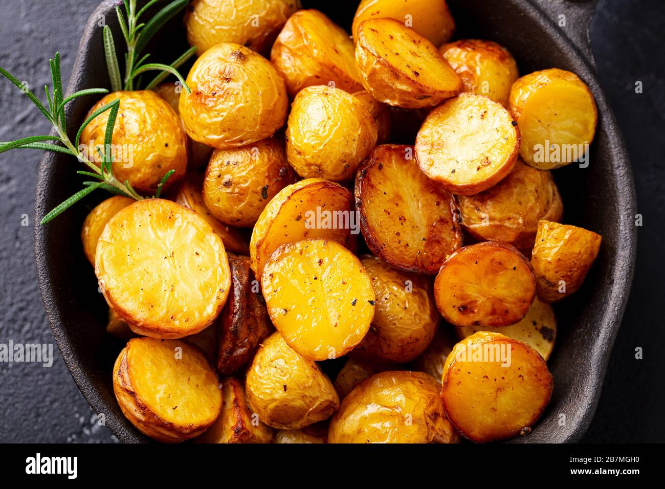 Roasted baby potatoes in iron skillet. Dark background. Close up. Stock Photo