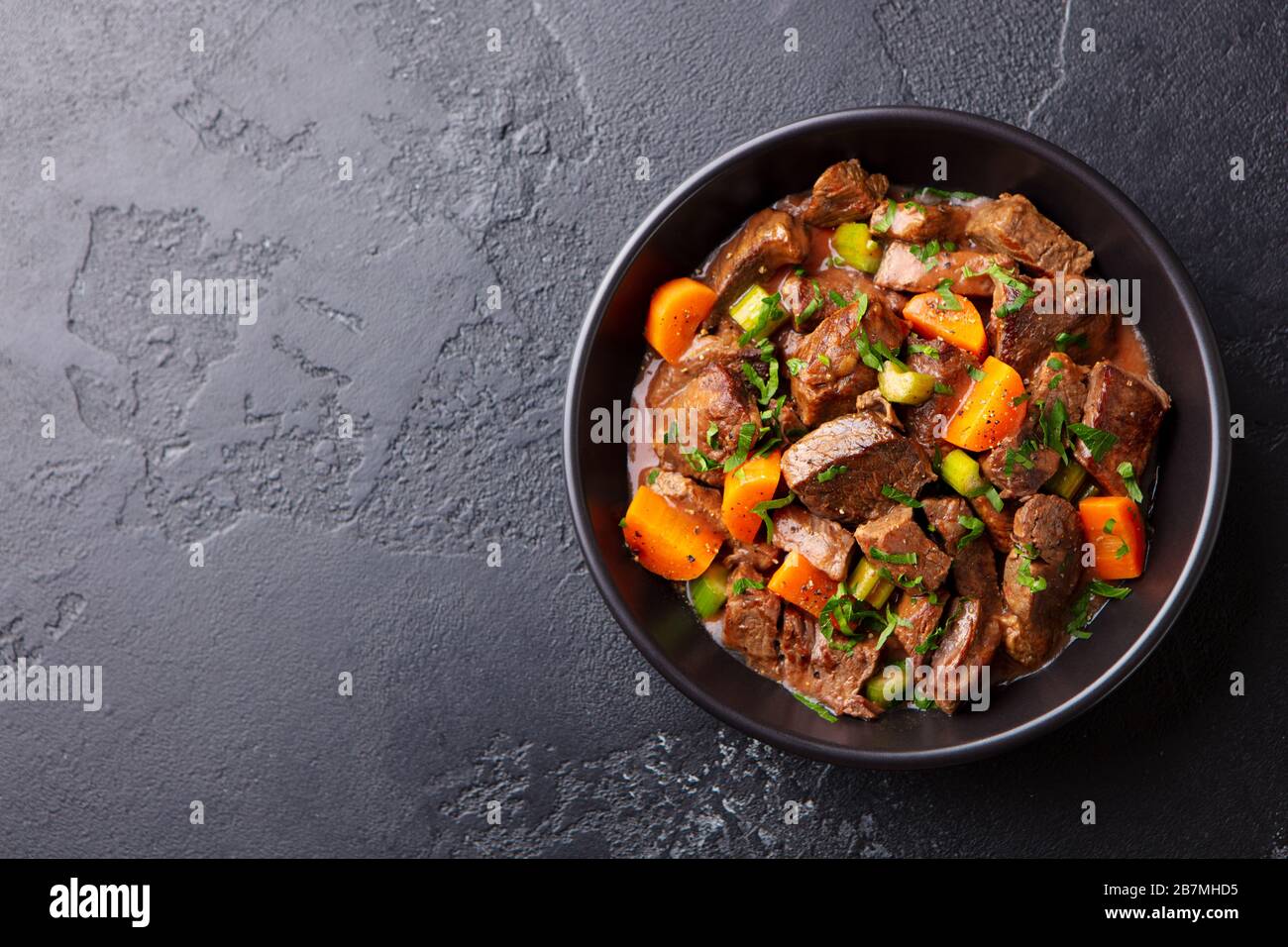 Beef meat and vegetables stew in black bowl. Dark background. Copy space. Top view. Stock Photo