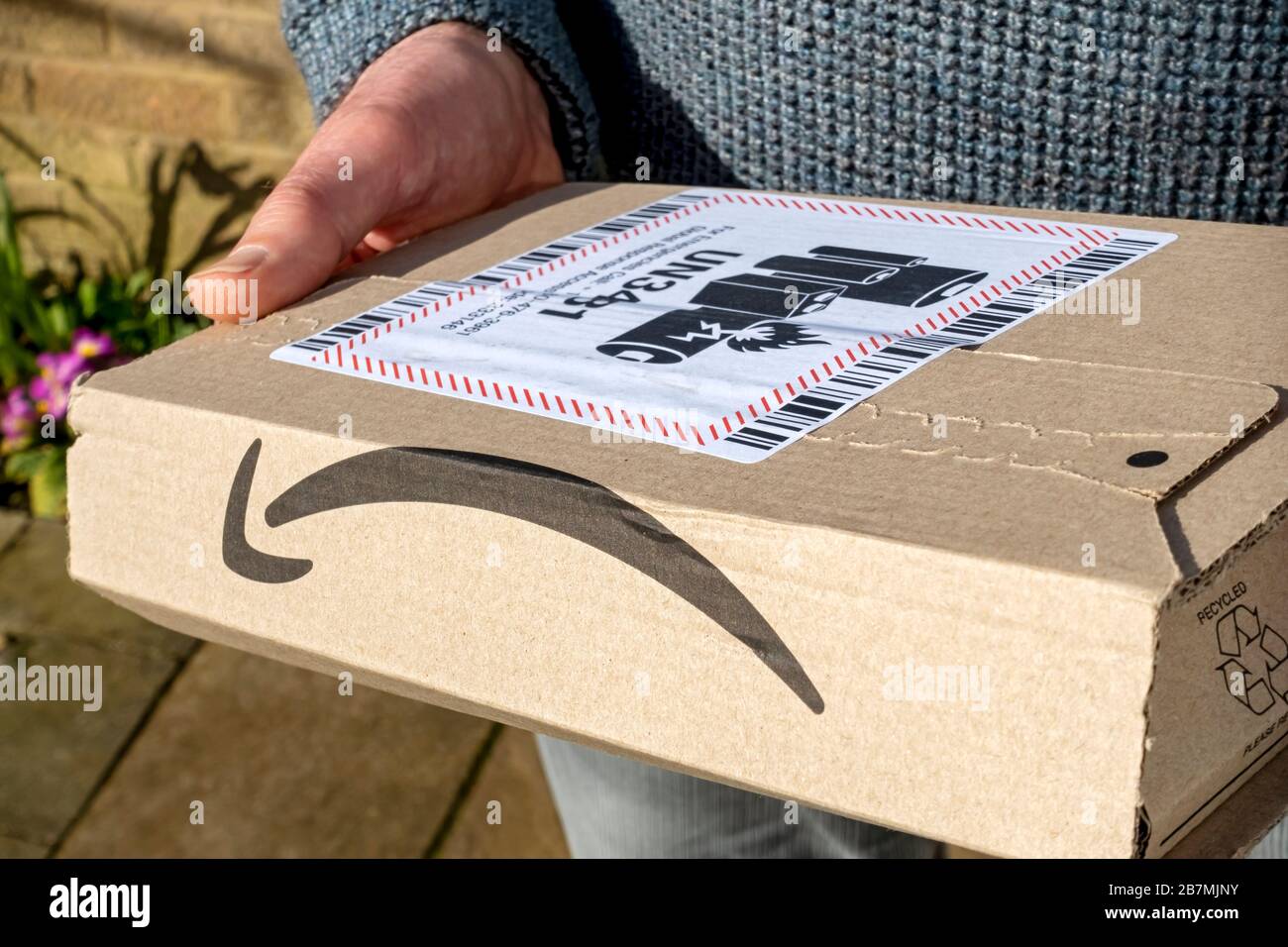 Close up of person man carrying holding online delivery Amazon box package delivery with lithium ion battery warning label England UK United Kingdom Stock Photo