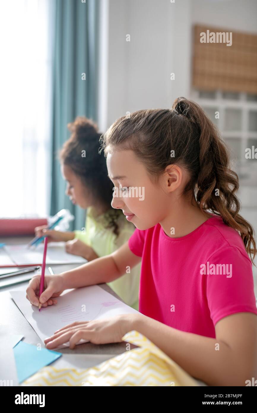Two girls of the same age drawing at the table. Stock Photo