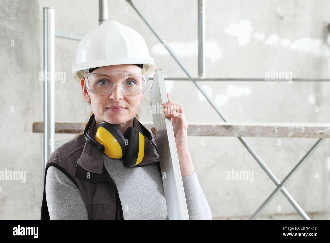 woman builder work with the straightedge spirit level, wearing helmet, safety glasses and