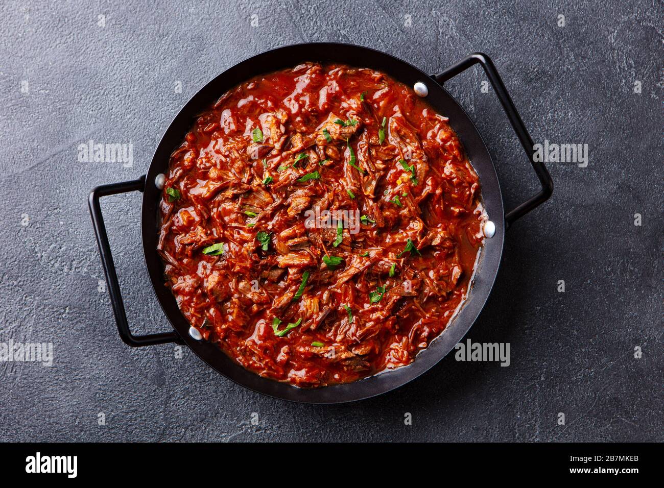 Beef shredded meat with sauce in black pan. Grey background. Close up. Top view. Stock Photo