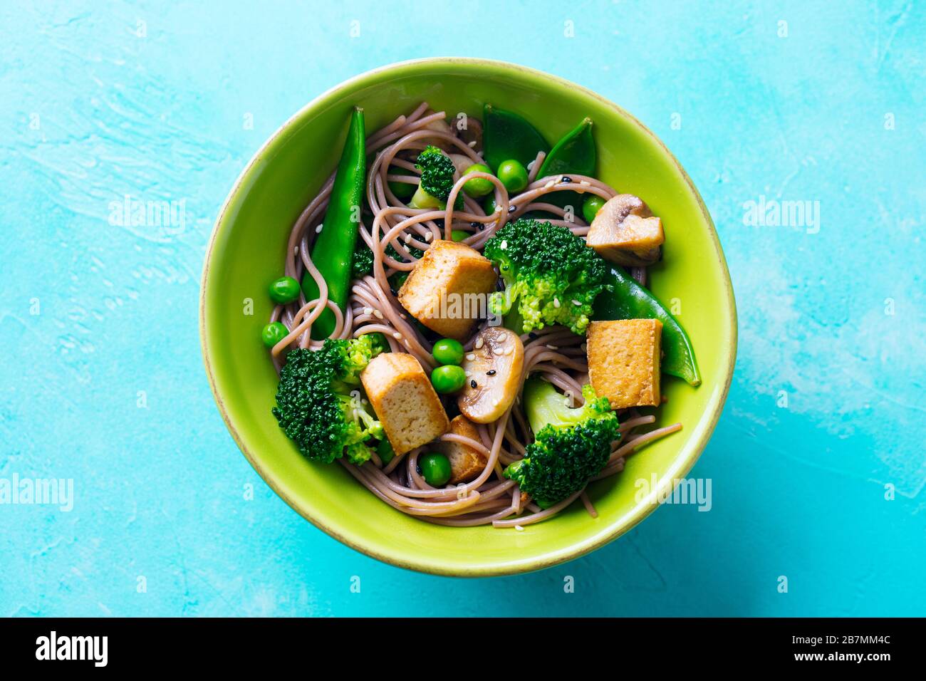 Soba noodles with vegetables and fried tofu in a bowl. Blue background. Close up. Top view. Stock Photo