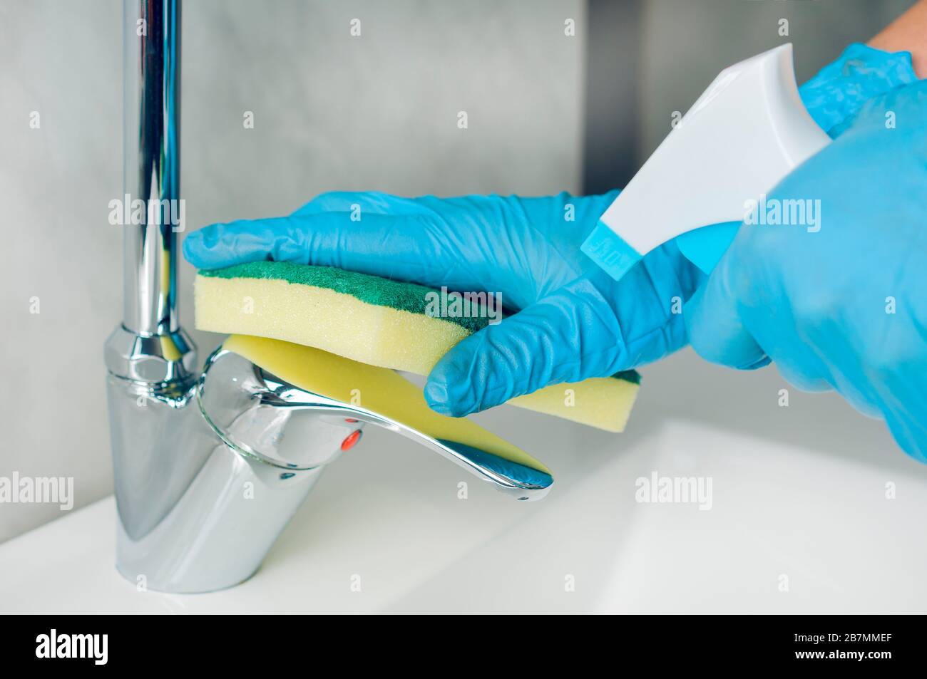 Woman with blue nitrile gloves disinfects the sink mixer after washing her hands to avoid the proliferation of viruses and bacteria Stock Photo