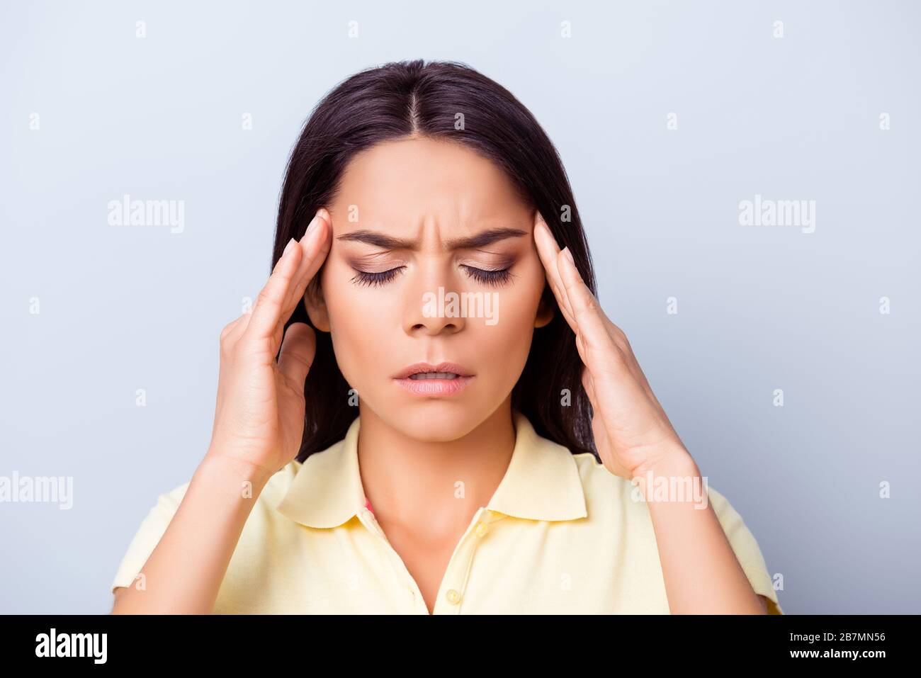 Close up portrait of a young pretty hispanic woman having headache after stressful workday and touching her temples Stock Photo