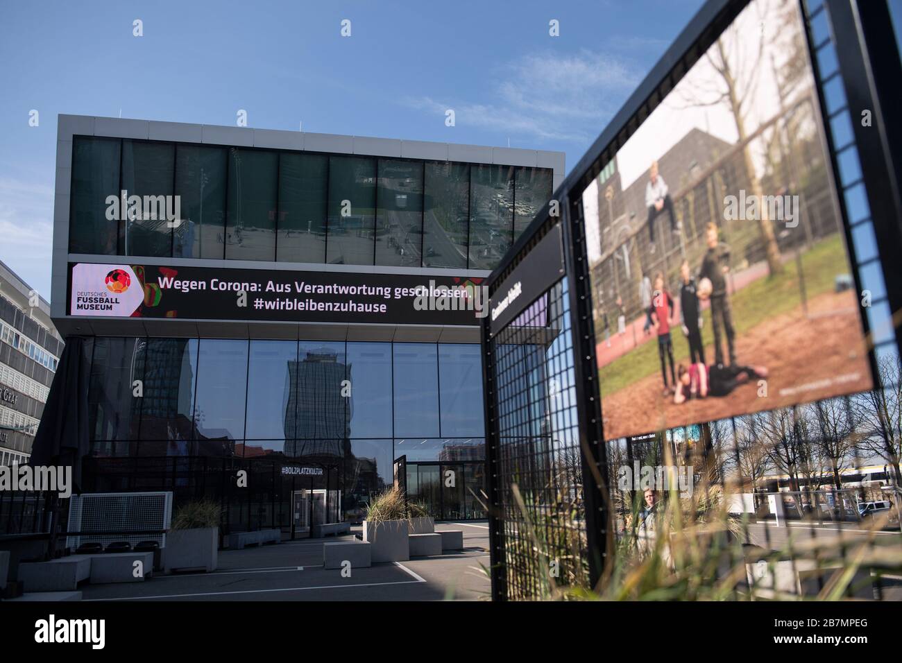 Dortmund, Germany. 17th Mar, 2020. The German Football Museum of the DFB writes on its LED band on the facade 'Wegen Corona: Aus Verantwortung geschlossen. #wirbleblezuhause', while a permanent exhibition on the forecourt shows a photo by Jörg Krüll showing five boys on a football field. Credit: Bernd Thissen/dpa/Alamy Live News Stock Photo