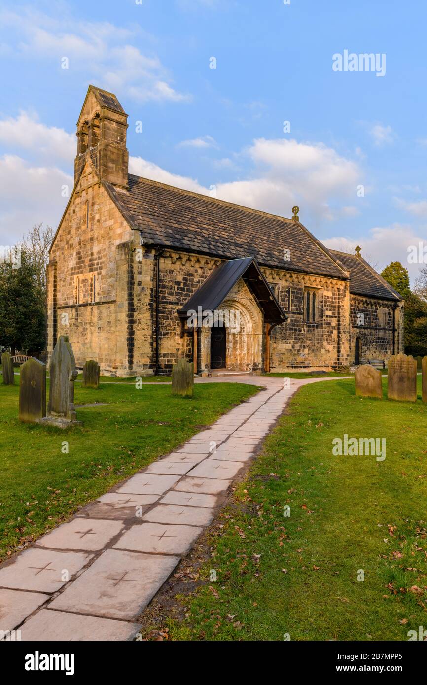 Exterior of historic Church of St John the Baptist, churchyard memorials & pathway leading to carved Norman doorway arch - Adel, Yorkshire, England UK Stock Photo