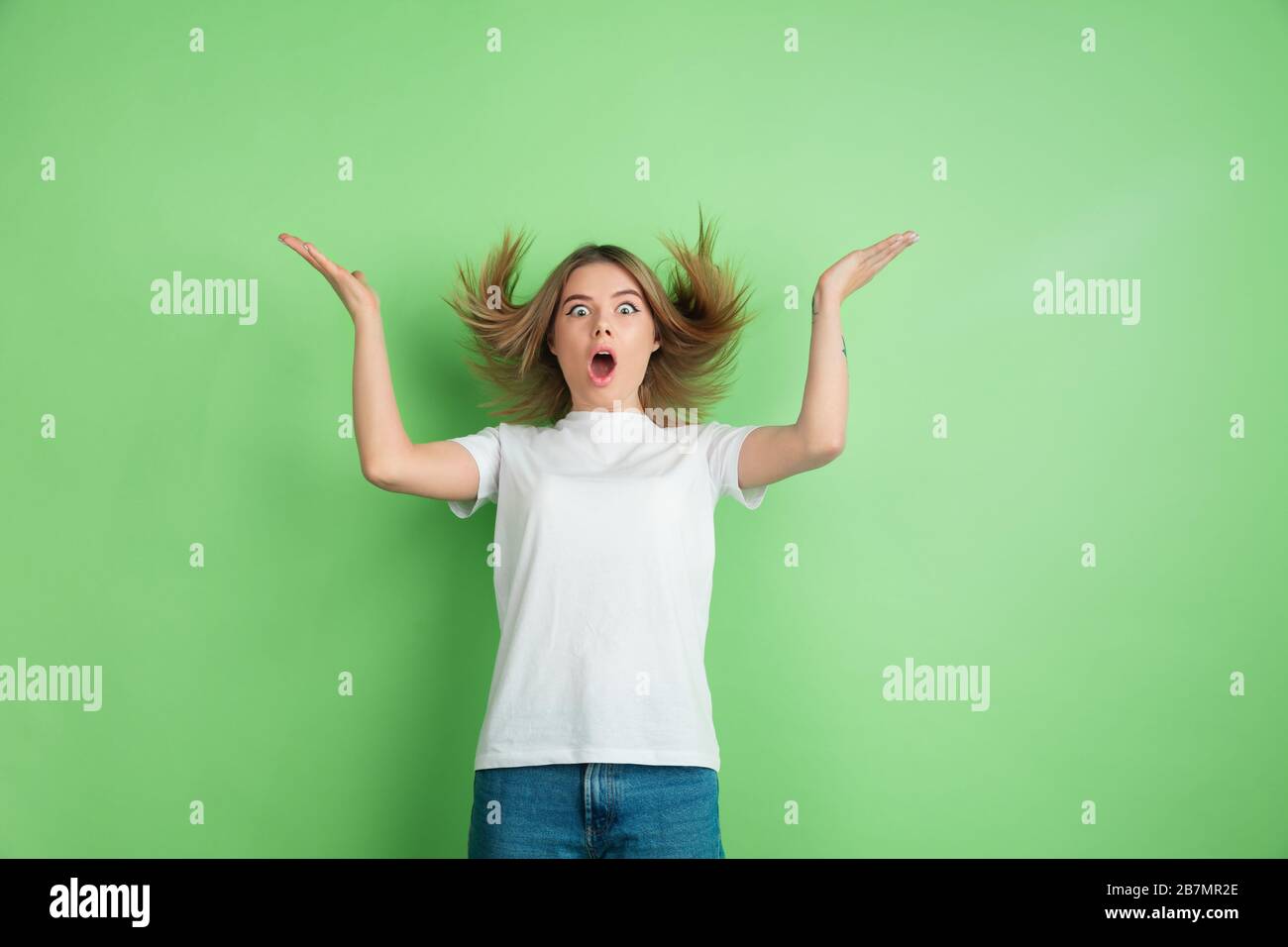 Surprised, astonished Caucasian young woman's portrait on green studio ...