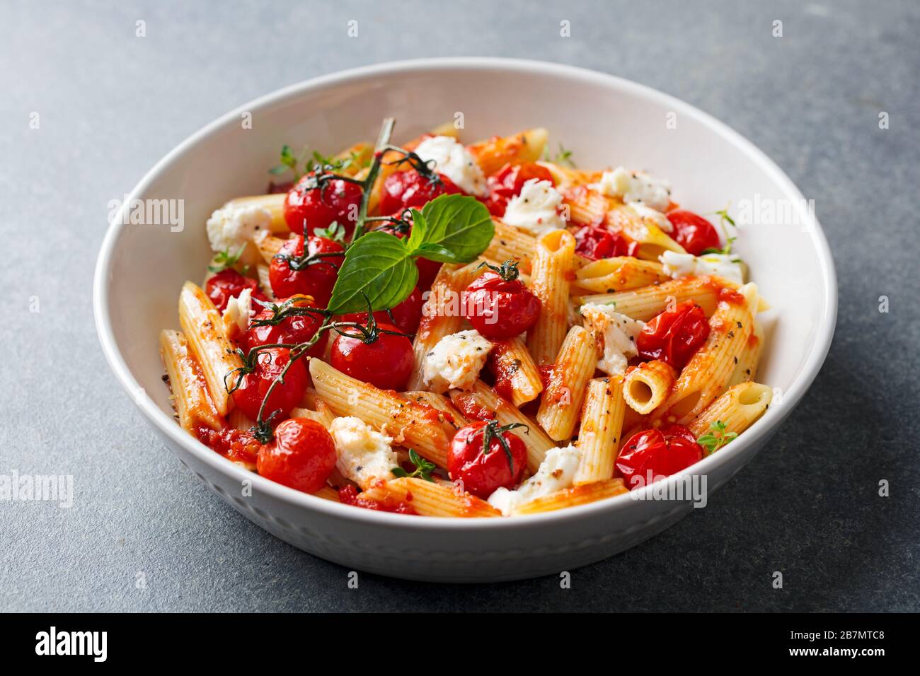 Pasta penne with roasted tomato, sauce, mozzarella cheese. Grey background. Close up. Stock Photo