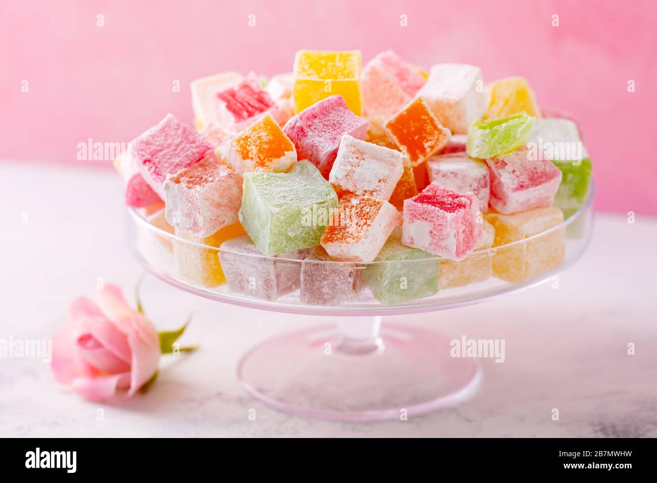Assorted Turkish delights on glass cake stand. Pink background. Close up. Stock Photo