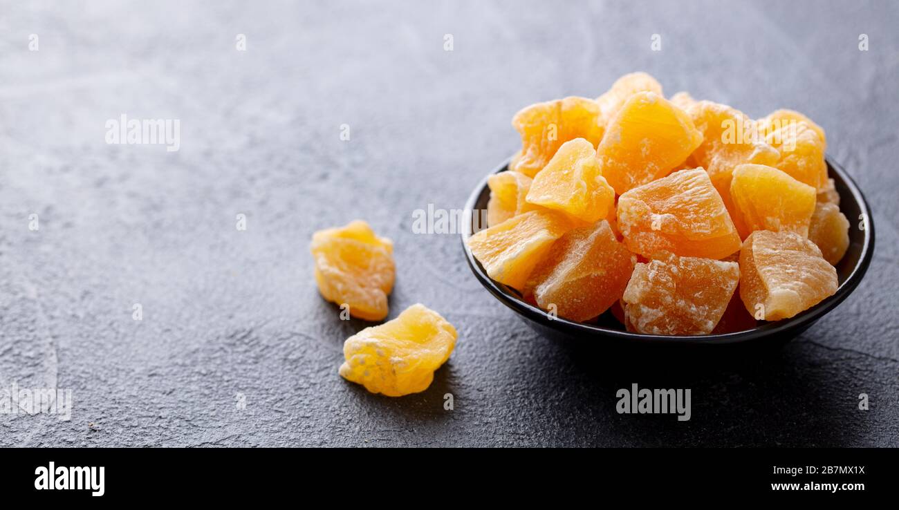 Candied ginger in black bowl on dark stone background. Copy space. Stock Photo