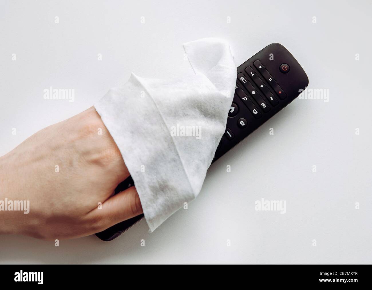 Close up view of man hand using antibacterial wet wipe for disinfecting home TV remote control. Stock Photo