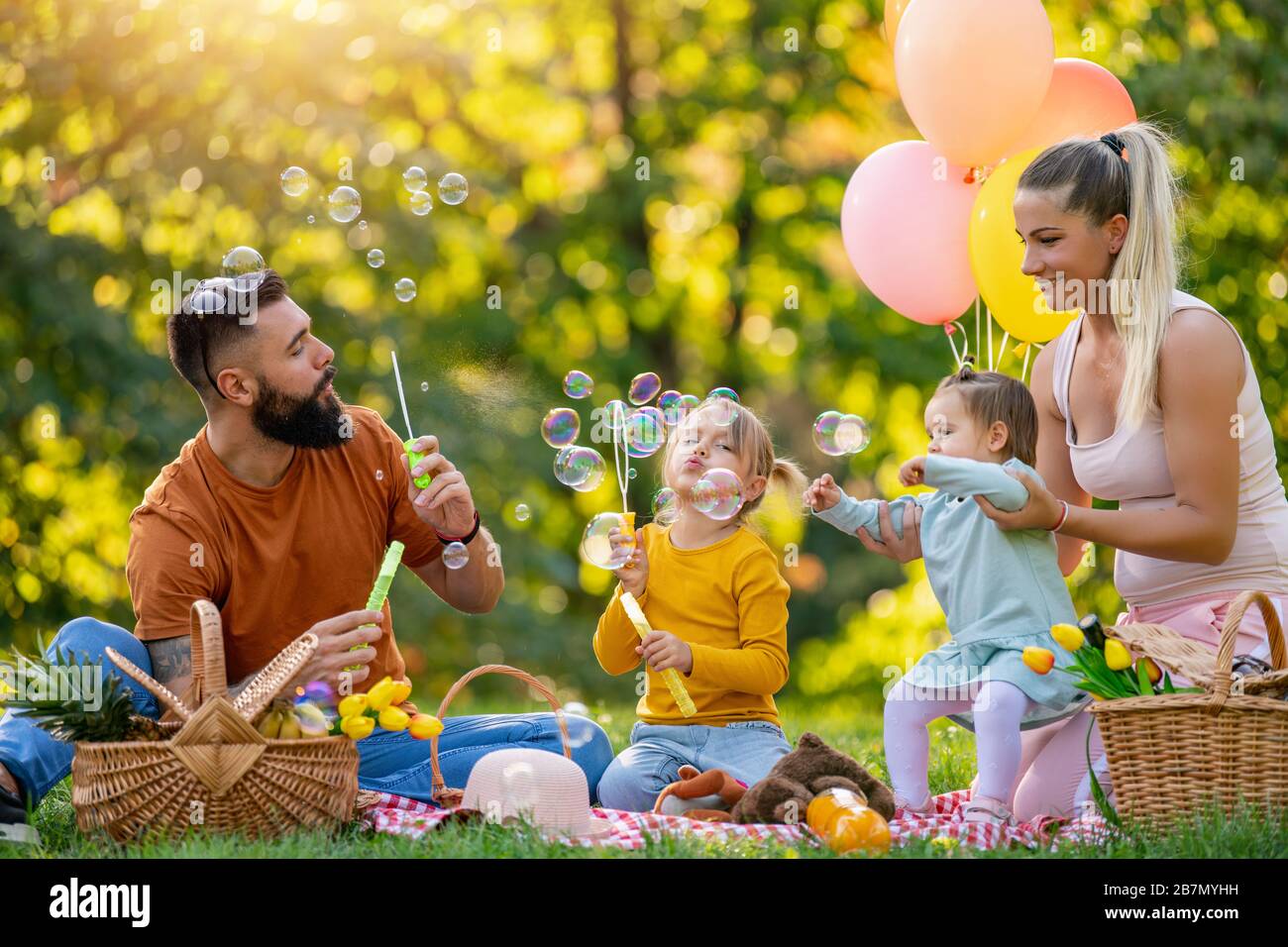 Happy family in the park together on a sunny day-they are blow soap bubbles.Family is enjoying a day in the park.Mother,father and children picnicking Stock Photo