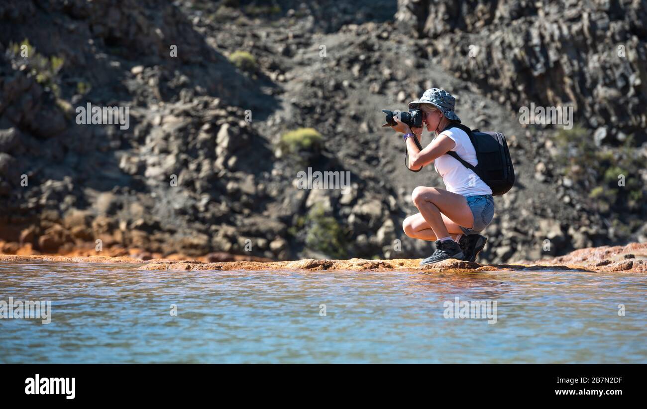 A photographer with DSLR camera walking by the river and mountains. Stock Photo