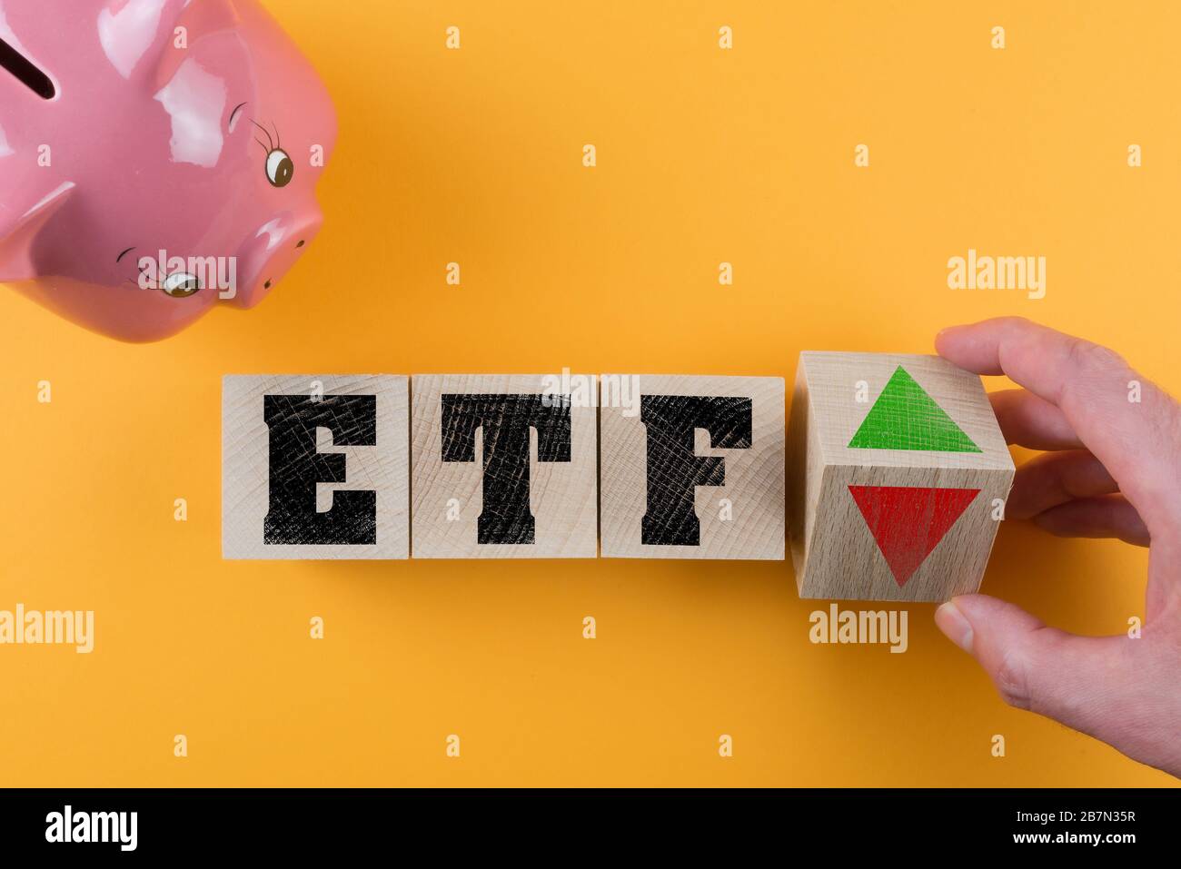 ETF exchange traded fund and red and green arrow symbol on wood cubes besides piggy bank on colored background, investing money concept Stock Photo