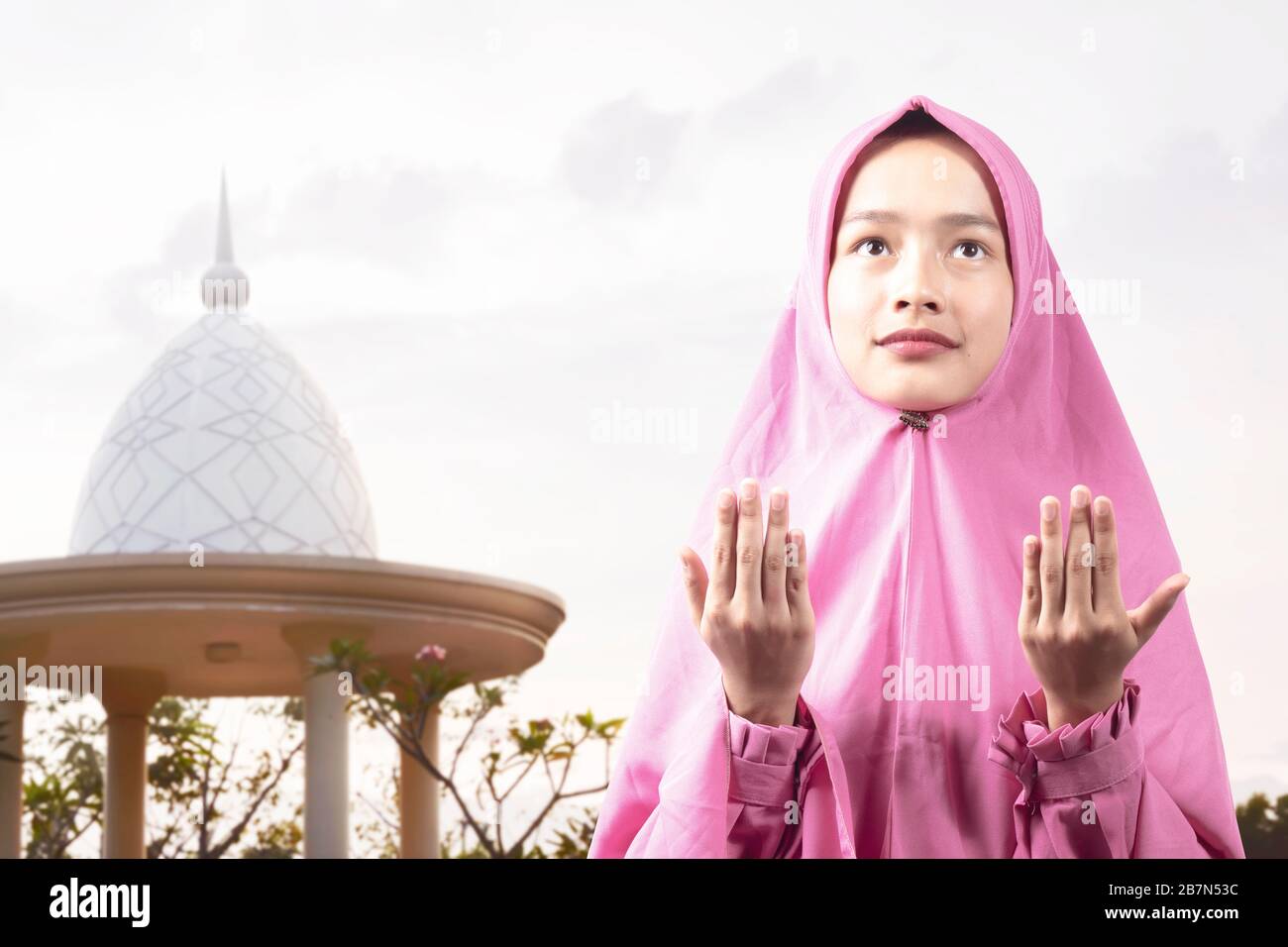 Asian Muslim woman in a veil standing while raised hands and praying ...